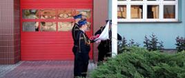 Strażacy w mundurach wyjściowych zakładają flagę państwową.