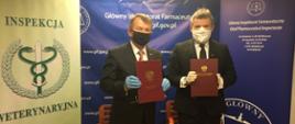 Główny Lekarz Weterynarii i Główny Inspektor Farmaceutyczny trzymają w dłoniach podpisane teczki z porozumieniem.