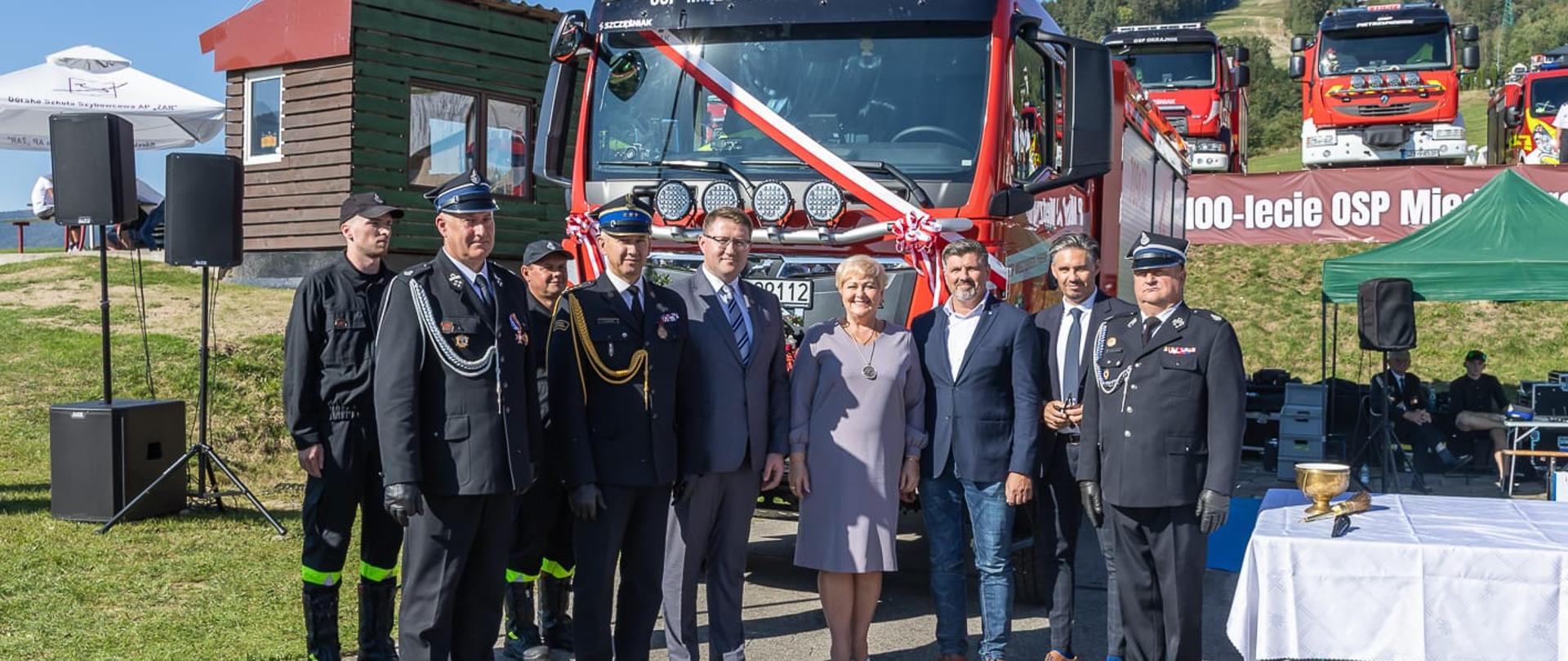 Zaproszeni goście a w tle nowy samochód ratowniczo-gaśniczy.