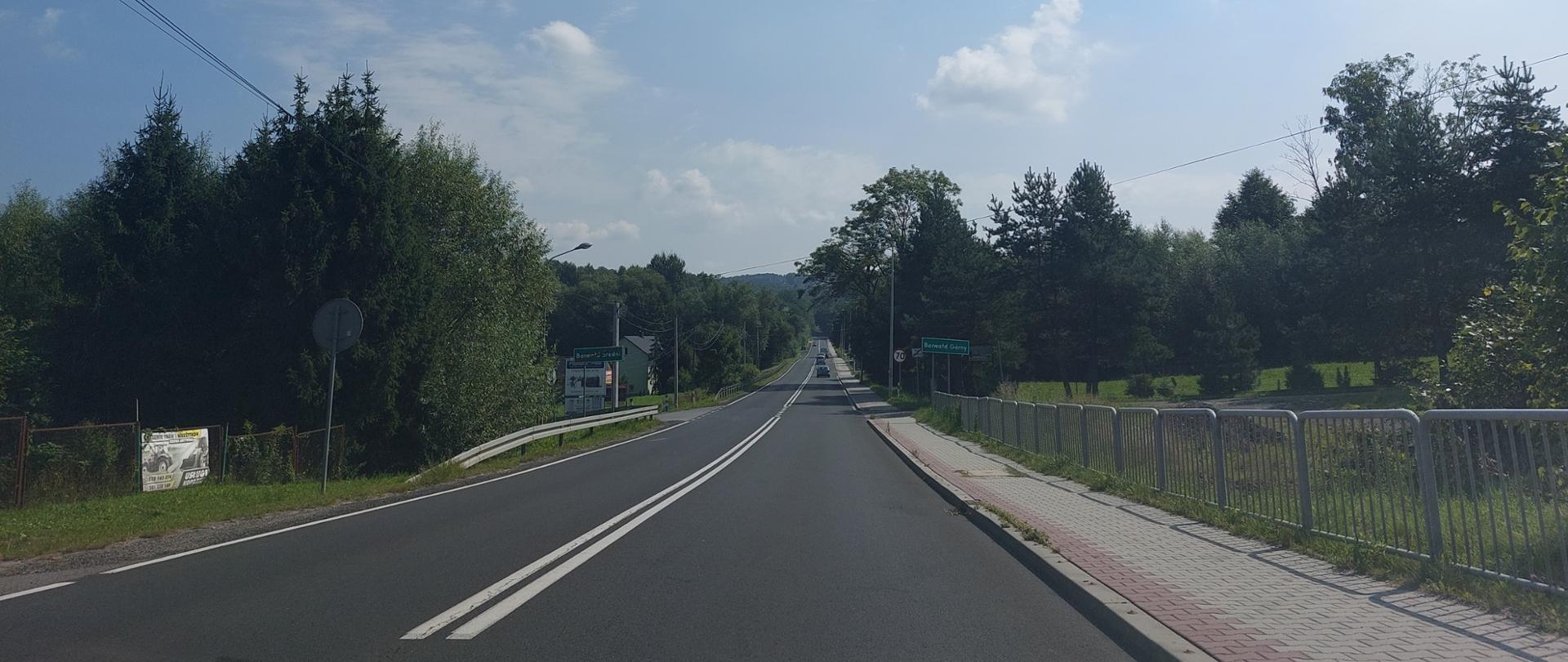 DK52 w Kleczy Górnej, wokół drogi roślinność i pojedynce zabudowania, po prawej chodnik