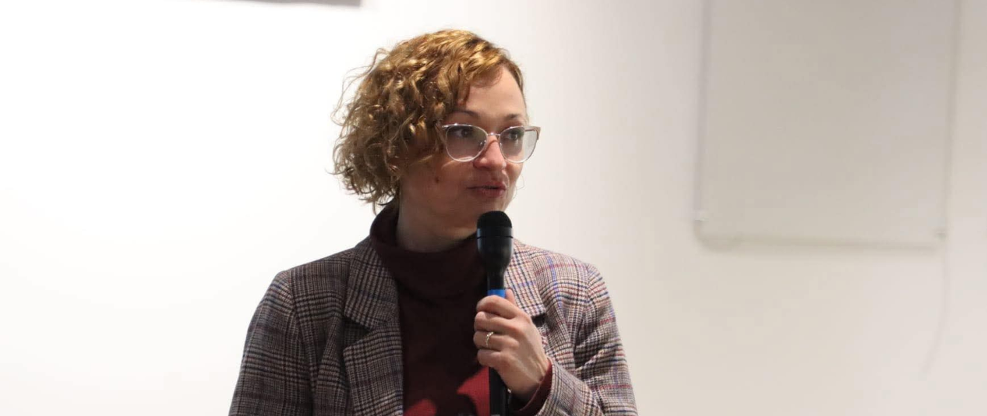 Wizerunek Zastępcy Regionalnego Dyrektora Ochrony Środowiska w Olsztynie, Regionalnego Konserwator Przyrody w Olsztynie. Kobieta stoi, w ręku trzyma mikrofon