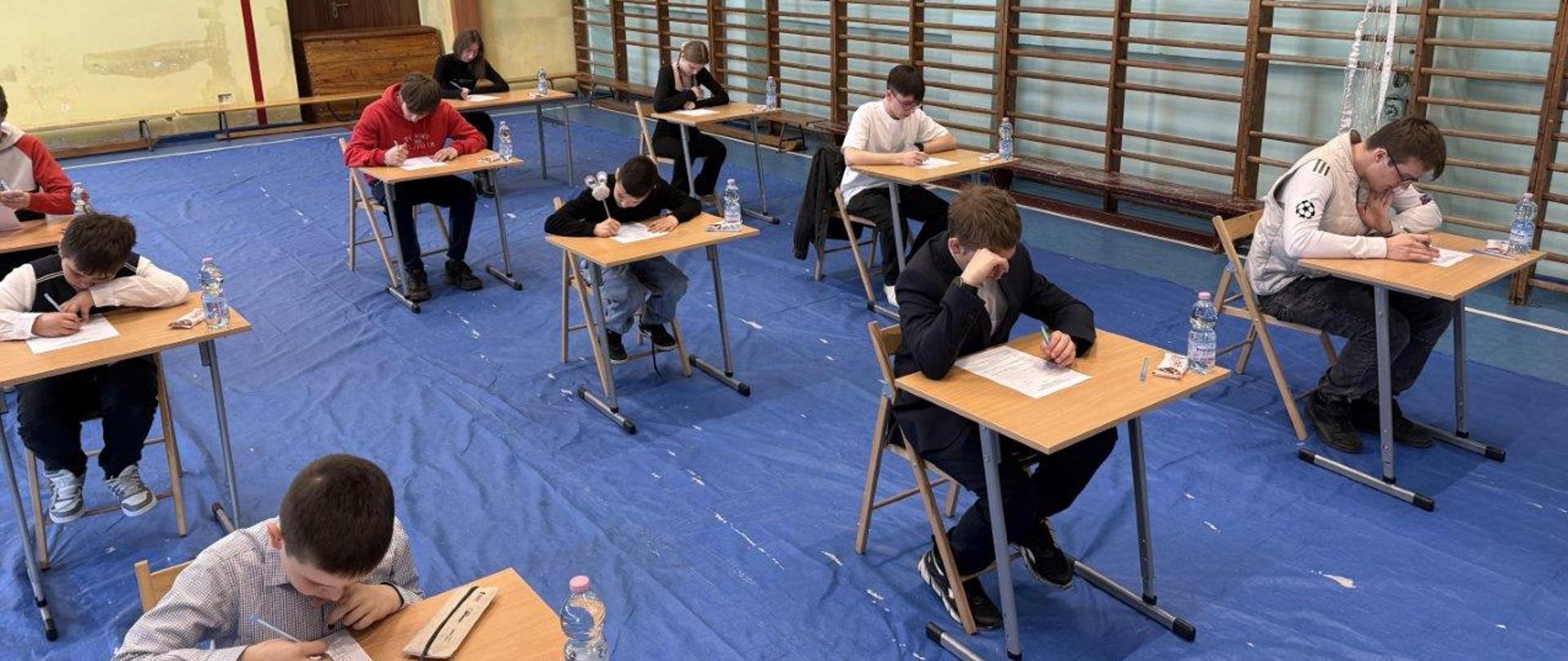 Widoczne są osoby siedzące w ławkach rozwiązuję test OTWP.