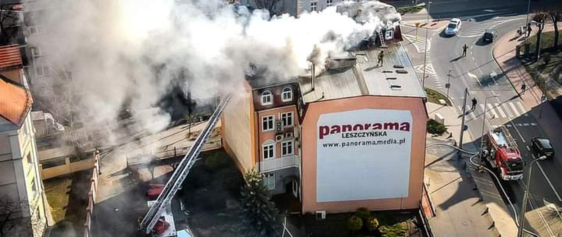 Dym wydobywający się z dachu budynku. Obok strażacka drabina mechaniczna.