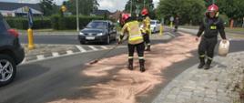 Zdjęcie przedstawia neutralizację przez strażaków plamy oleju na drodze wojewódzkiej nr 163 w Białogardzie. Strażacy szczotkują nawierzchnię jezdni