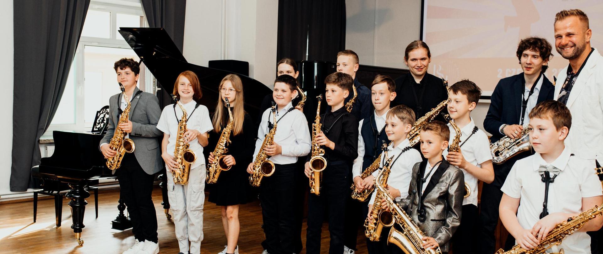 Zdjęcie przedstawiające wykonawców popisu klasy saksofonu pana Mateusza Boducha, który odbył się 2 czerwca 2025 roku w auli szkoły.