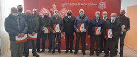 Zdjęcie przedstawia strażaków oraz druhów OSP, którzy otrzymali od komendanta decyzje o przyznaniu świadczenia ratowniczego, Strażacy oraz druhowie stoją przed banerem komendy. 