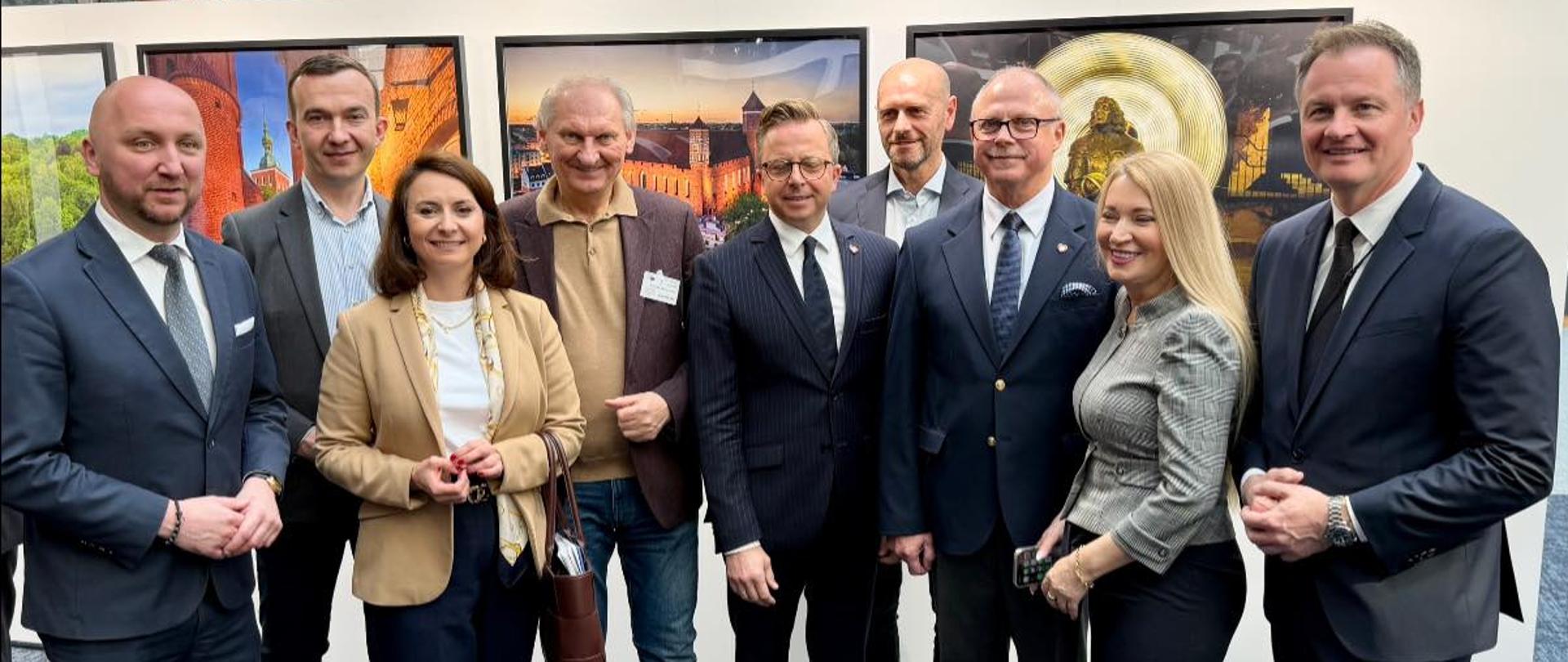 Grupa oficjeli pozuje do zdjęcia na tle obrazów