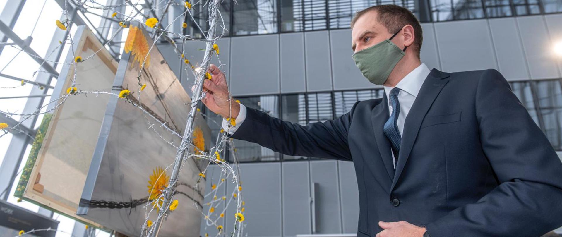 Ambasador Szatkowski przypina symboliczny kwiat do instalacji artystycznej