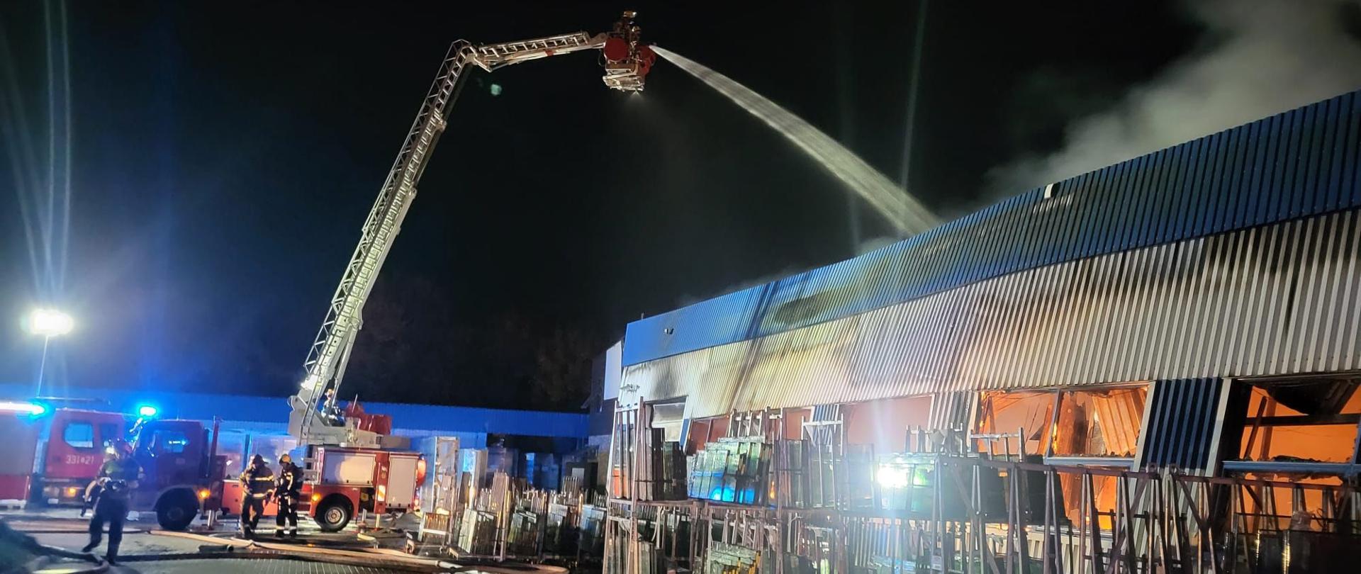 Na zdjęciu strażacy leją wodę na pożar we wnętrzu hali z kosza podnośnika 