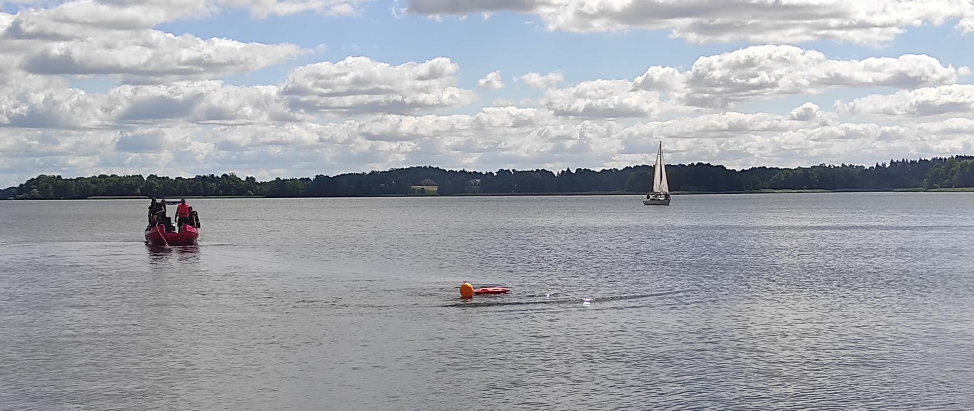 Zdjęcie przedstawia łódź strażacką podczas asekuracji ratownika w wodzie, który właśnie wykonuje nurkowanie ratownicze