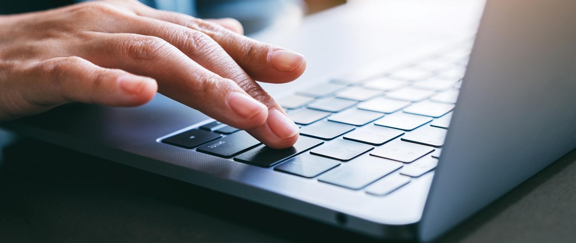 Dłoń na klawiaturze laptopa. 