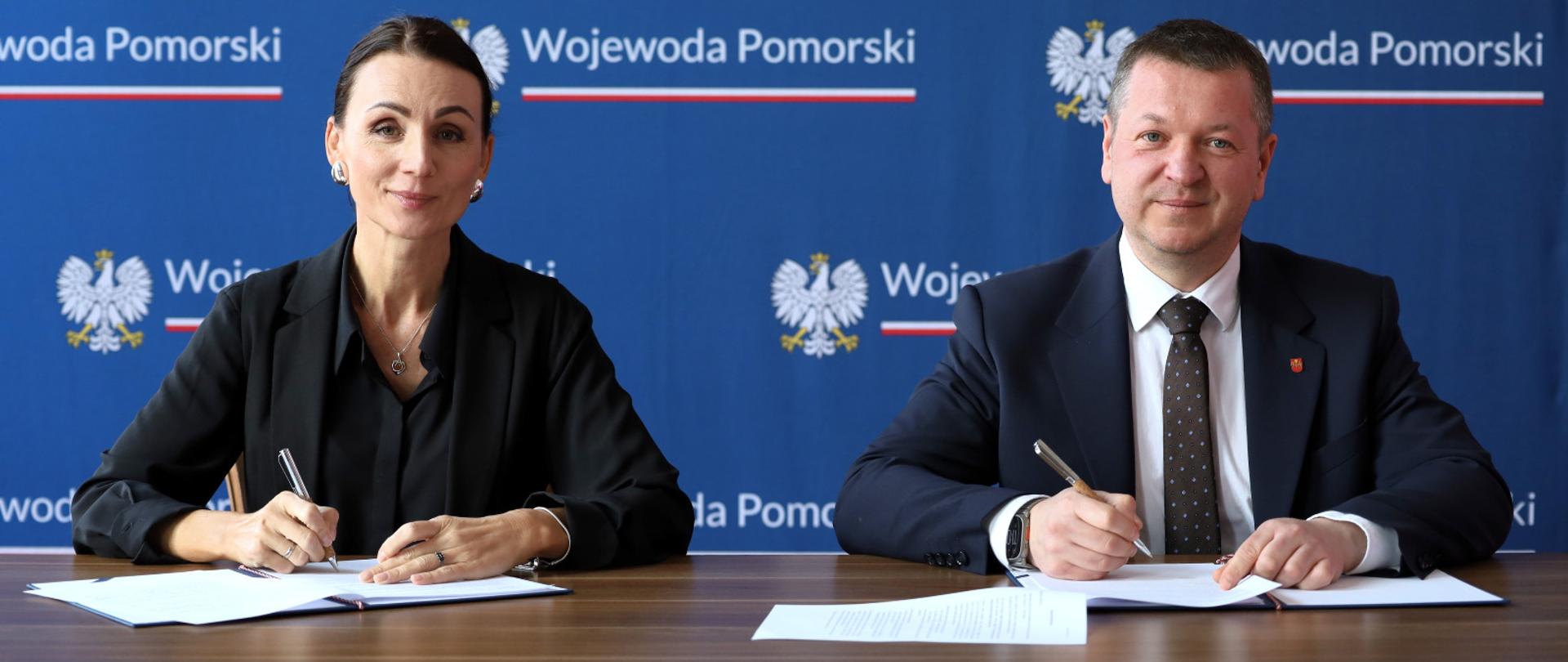 dwie osoby kobieta i mężczyzna podpisują umowę, w tle napis wojewoda pomorska