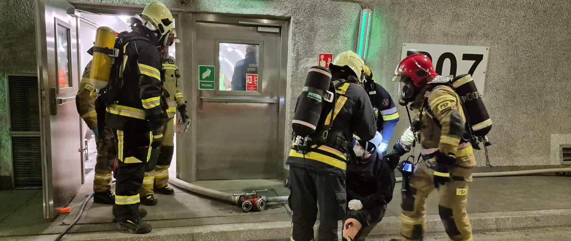 Strażacy w tunelu podczas ćwiczeń, niosą rannego do przejścia ewakuacyjnego