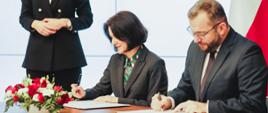 Minister funduszy i polityki regionalnej Grzegorz Puda i dyrektor Centrum Unijnych Projektów Transportowych Joanna Lech podpisują porozumienie w sprawie realizacji wybranych zadań z programu Fundusze Europejskie na Infrastrukturę, Klimat, Środowisko 2021–2027, dyrektor i minister siedzą przy stole i podpisują dokumenty