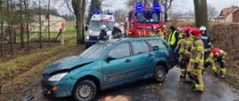 Uszkodzony pojazd marki Ford stoi na jezdni w tle strażacy policjant oraz pojazdy ratownicze