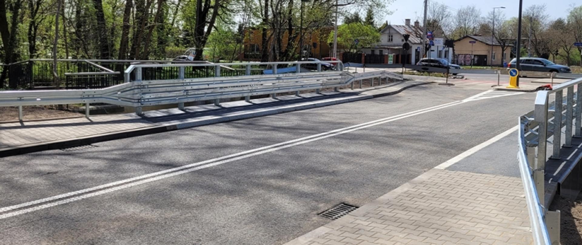 Niewielki most nad rzeczką, w oddali poruszające się samochody.