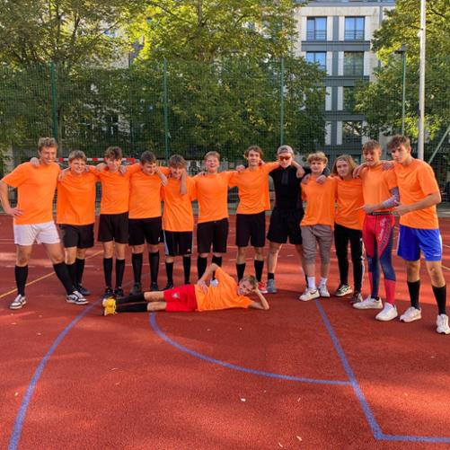 zdjęcie przedstawia drużynę w pomarańczowych koszulkach podczas wspólnego pozowanego zdjęcia po meczu, jeden z zawodników leży na boisku