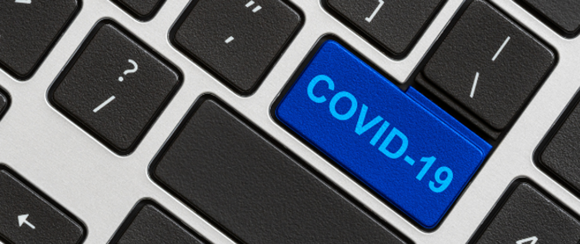 Grafika dekoracyjna: fagment klawiatury komputerowej z czarnymi klawiszami na jasno szarym tle. Zamiast strzałki dla niebieskiego klawisza Enter błękitny napis COVID-19 .