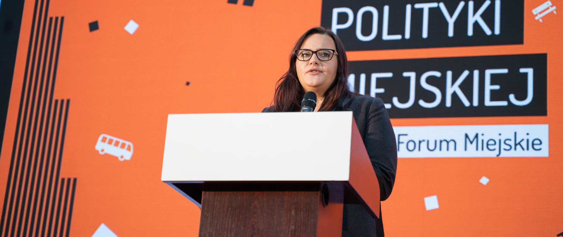 Minister Małgorzata Jarosińska-Jedynak stoi przy mównicy za nią wyświetlony jest napis Kongres Polityki Miejskiej 