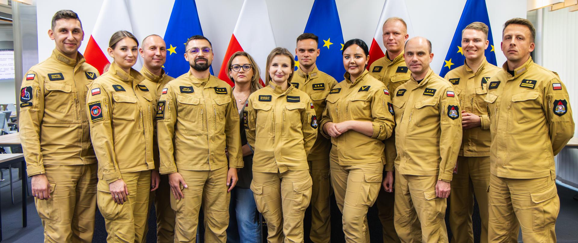 Na zdjęciu wewnątrz sali konferencyjnej widoczni są strażacy, którzy pozują do zdjęcia grupowego. Wszyscy ubrani są w mundury służbowe w kolorze piaskowym.