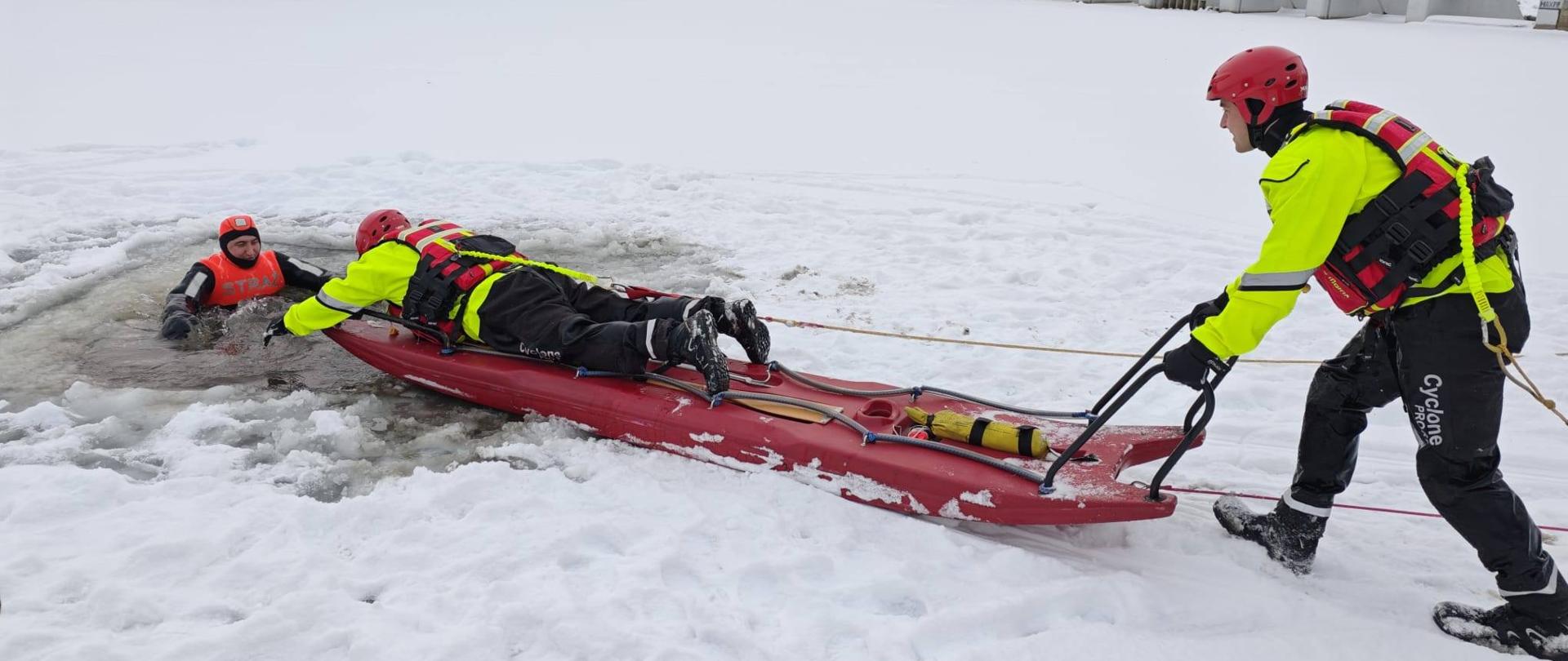 Dzień. Na zamarzniętym akwenie, ratownicy w jaskrawych strojach i czerwonych kaskach wydobywają osobę z przerębla. Jeden z ratowników leży na specjalnych saniach lodowych i podaje rękę poszkodowanemu, podczas gdy drugi ciągnie sanie liną z brzegu. Cała scena rozgrywa się w zimowym.