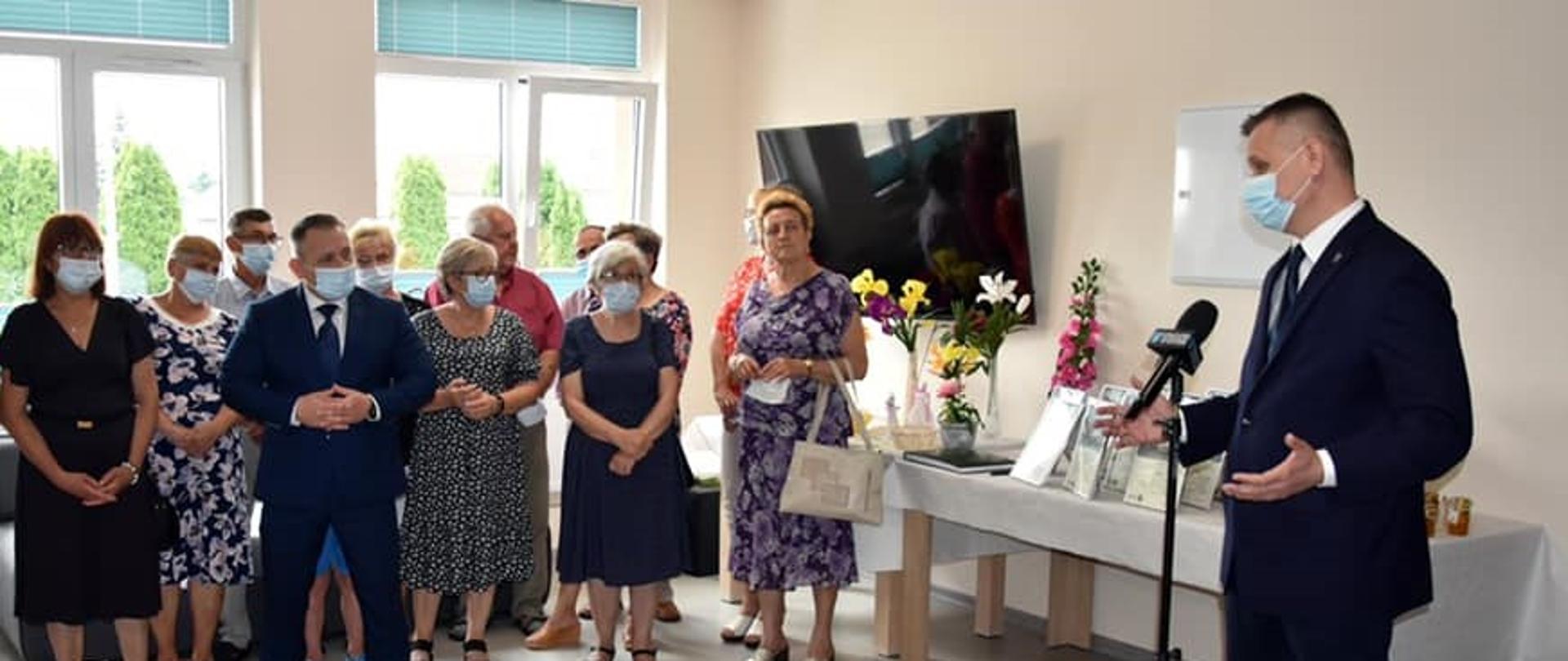 Grupa osób w sali słuchająca wystąpienia Wicewojewody Mazowieckiego Artura Standowicza.