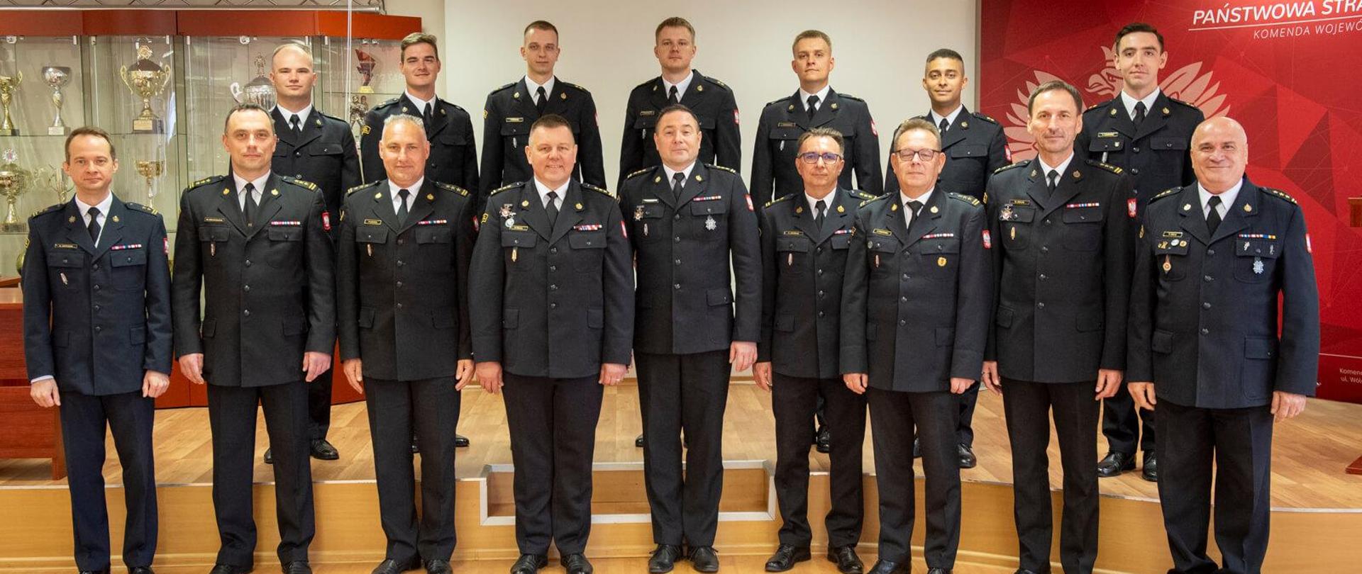 szesnastu strażaków pozujących do zdjęcia stoją w dwóch rzędach w sali konferencyjnej