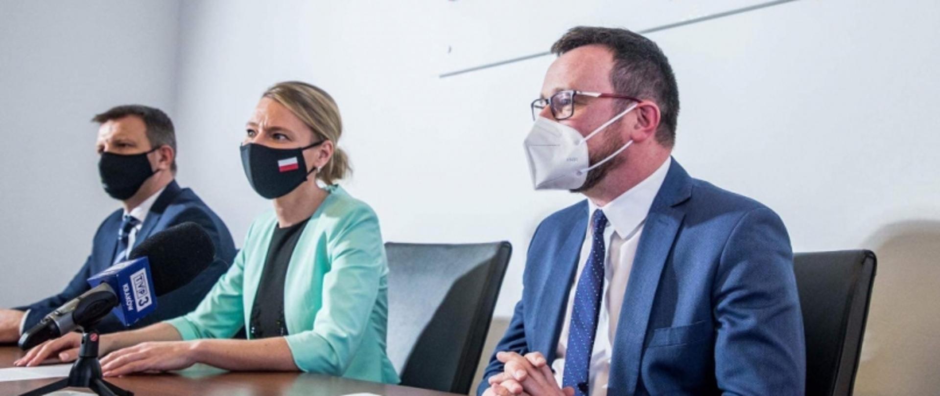 Trzy osoby przy stole, mikrofon „TVP3” na pierwszym planie.