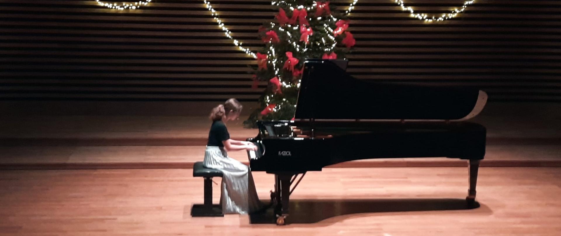 Nastolatka gra na fortepianie na estradzie sali koncertowej.