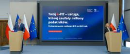 Dwie osoby stoją przy oddzielnych mównicach, a między nimi ekran z napisem „Twój e‑PIT – usługa, której zaufały miliony podatników” oraz informacją o podsumowaniu PIT za 2025 rok.