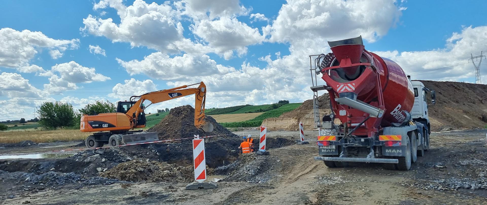 DK9 budowa obwodnicy Ostrowca Świętokrzyskiego - roboty ziemne, wykop, nasyp, czerwona betoniarka, pomarańczowa koparka, dwóch robotników w wykopie 