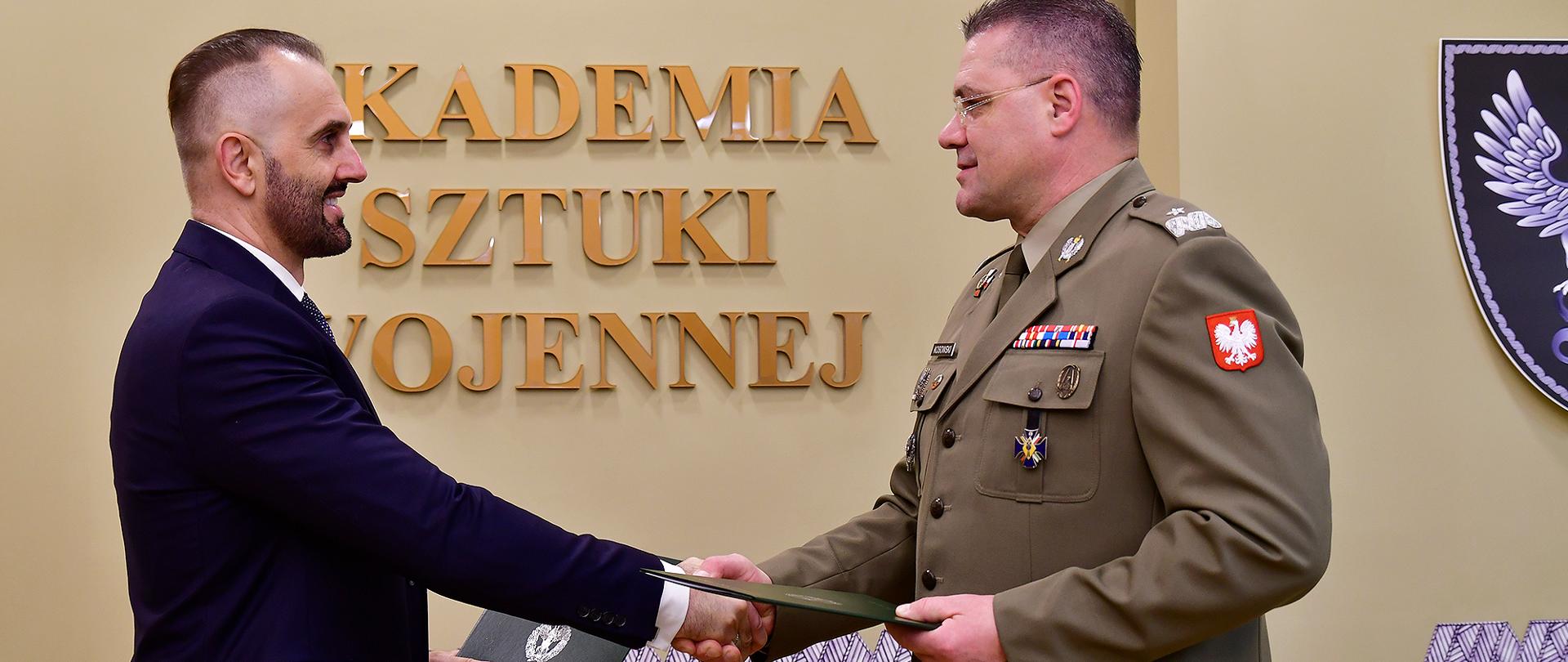 Porozumienie Rządowego Centrum Bezpieczeństwa i Akademii Sztuki Wojennej w sprawie organizacji szkolenia z zakresu zarządzania bezpieczeństwem narodowym. Zdjęcie przedstawia sygnatariuszy porozumienia. W tle "Akademia Sztuki Wojennej".
