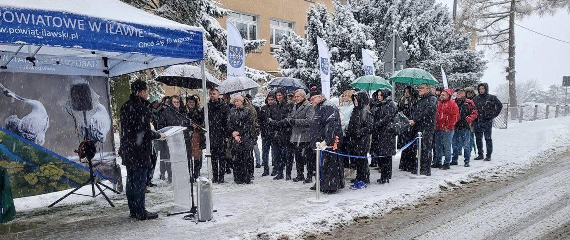 Kilkanaście osób stoi na drodze w plenerze zimowym 