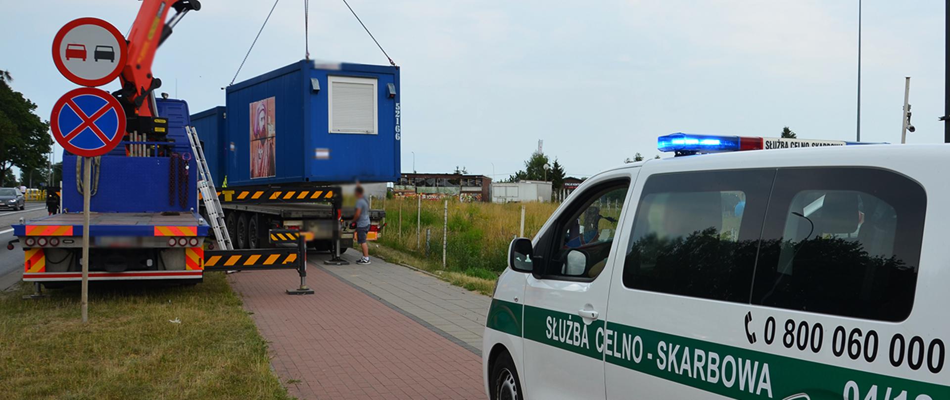 Radiowóz Służby Celno-Skarbowej, dźwig podczas ładowania kontenera na naczepę samochodu ciężarowego.