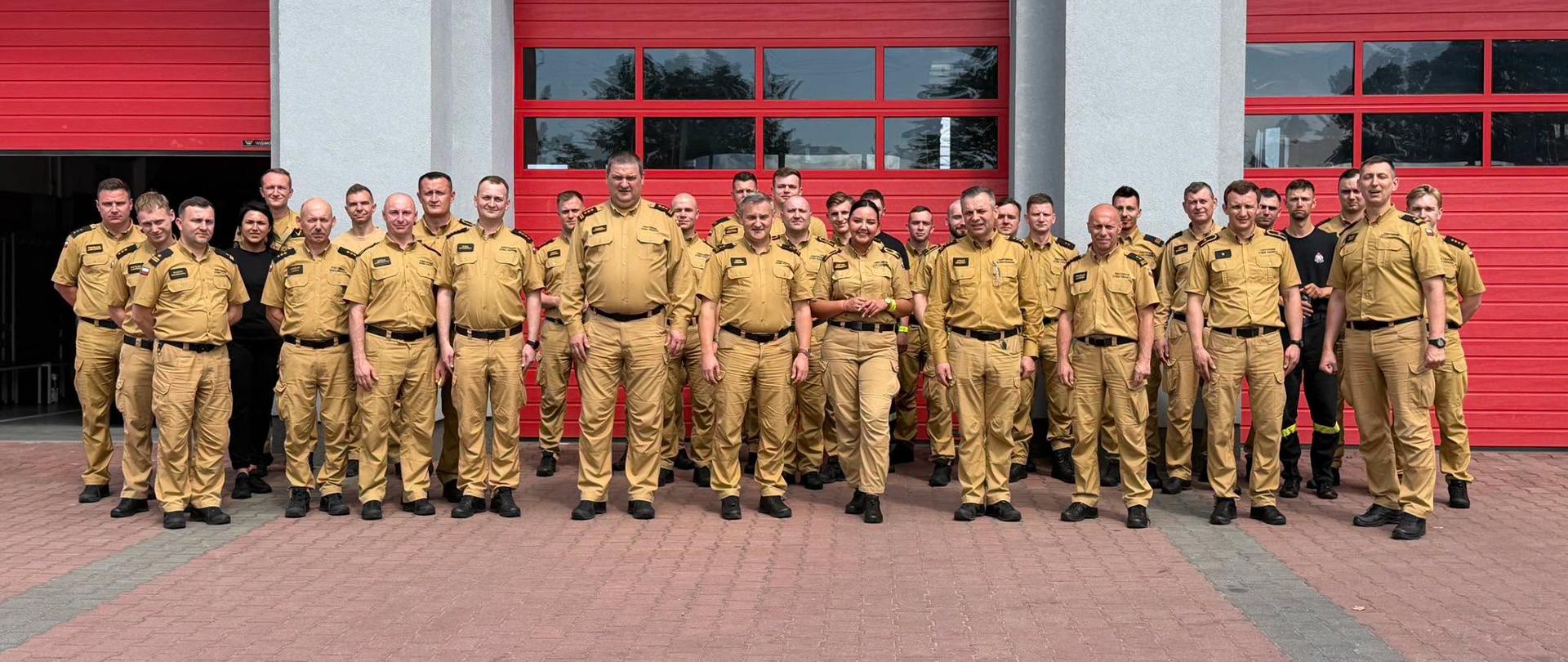 Dwudniowa odprawa szkoleniowa skierowana do funkcjonariuszy realizujących zadania z zakresu Prewencji Społecznej PSP - zdjęcie grupowe na tle bram garażowych PSP