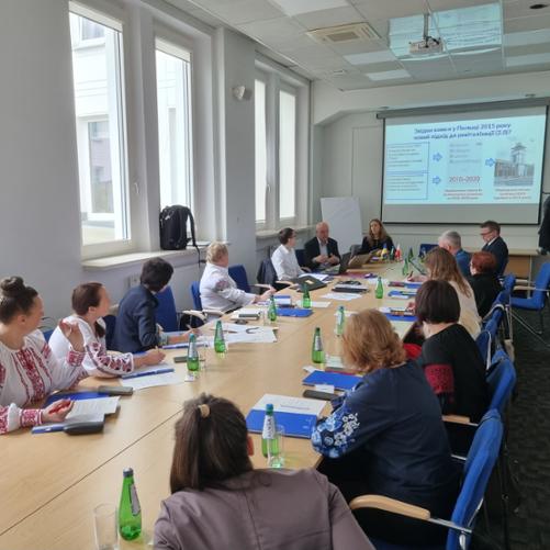 Grupa osób siedzi przy długim stole konferencyjnym patrząc na prezentację. Część kobiet ubranych jest w tradycyjne koszule ukraińskie. Na stole leżą notatki