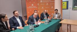 Stół nakryty zielonym materiałem, za stołem gości Dyrektor Oddziału podpisuje umowę
