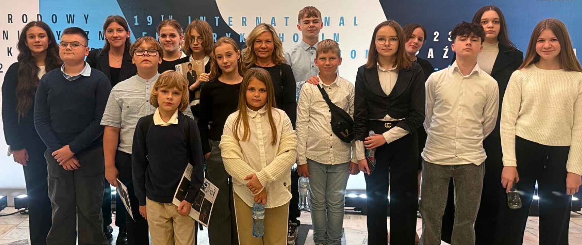 grupa kilkunastu osób stojących na tle baneru konkursu chopinowskiego