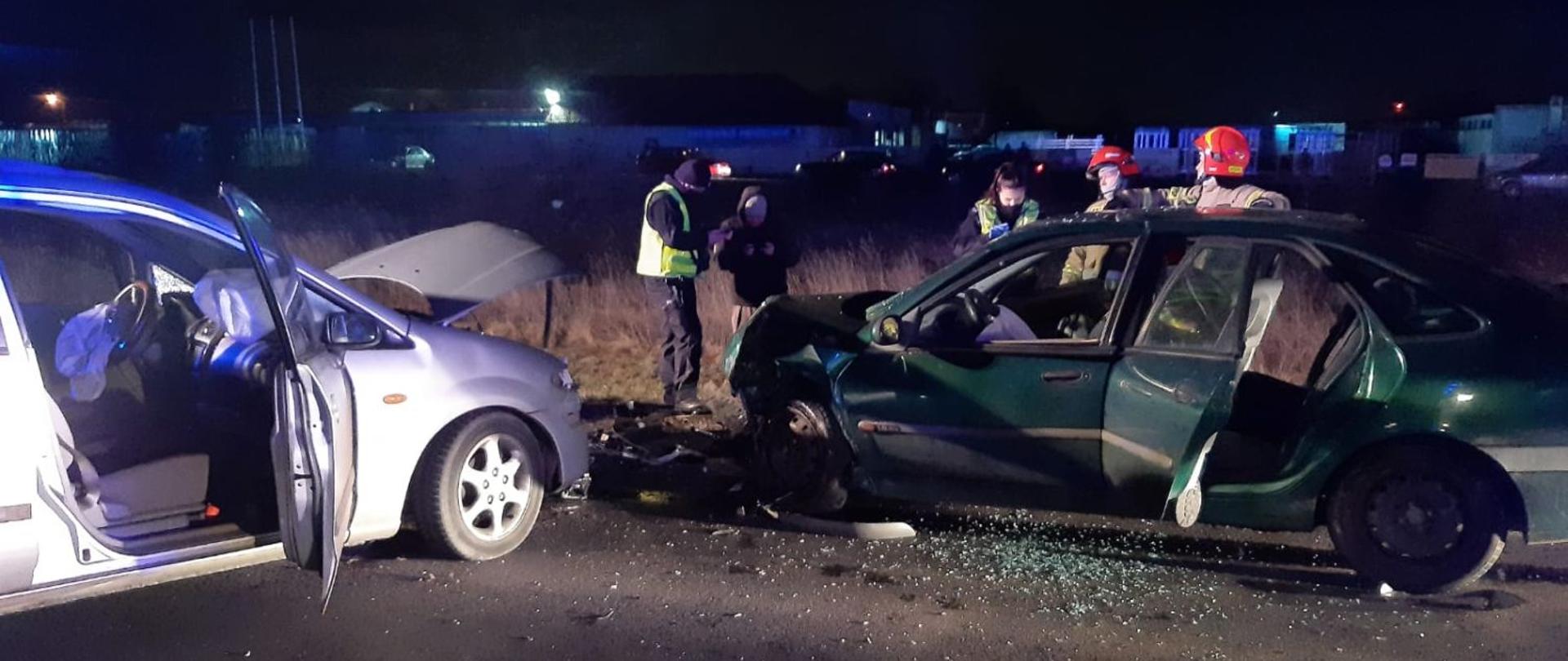 W porze nocnej prowadzone są działania strażaków Państwowej Straży Pożarnej i funkcjonariuszy Policji. Na drodze obwodnicy żarskiej po zderzeniu czołowym stoją dwa samochody osobowe Renault i Mazda. W wyniku zderzenia w obu pojazdach zadziałały poduszki bezpieczeństwa. Przy zielonym samochodzie marki Renault na drodze leżą odłamki zbitej szyby.