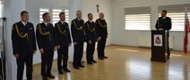Funkcjonariusze PSP w umundurowaniu galowym w szeregu, Komendant za mównicą, Komendant wita na uroczystości funkcjonariusza przechodzącego na zaopatrzenie emerytalne