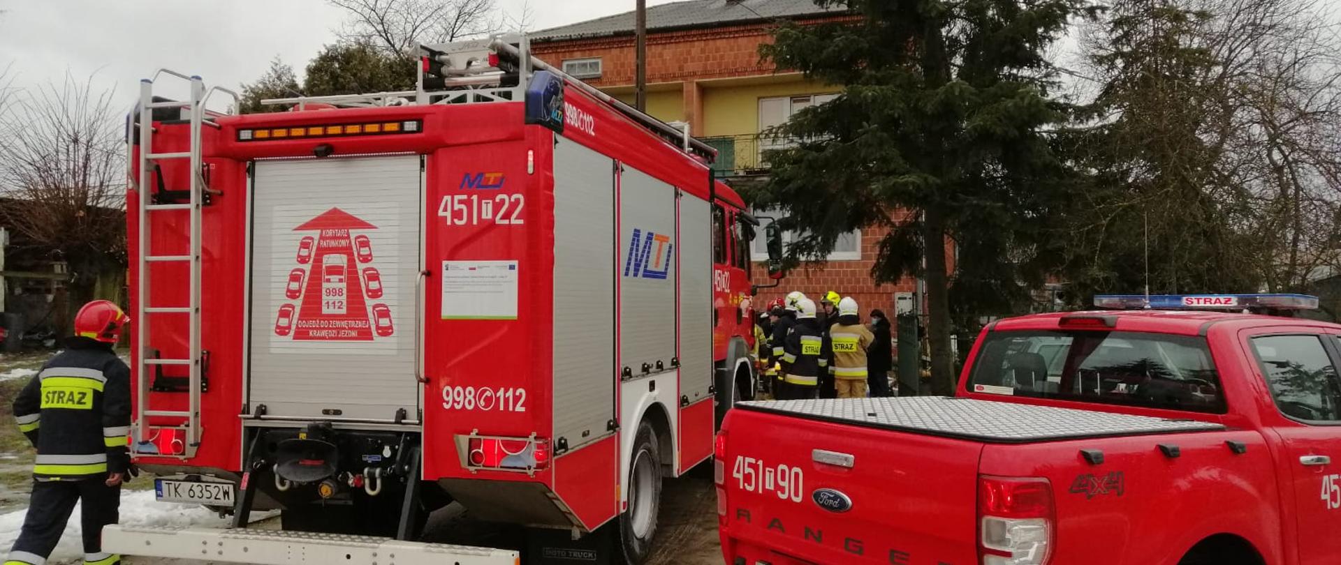 Przed posesją do, której doszło do wybuchu gazu stoją samochody strażackie wraz z ratownikami. Na dalszym planie widać dom murowany z cegły.