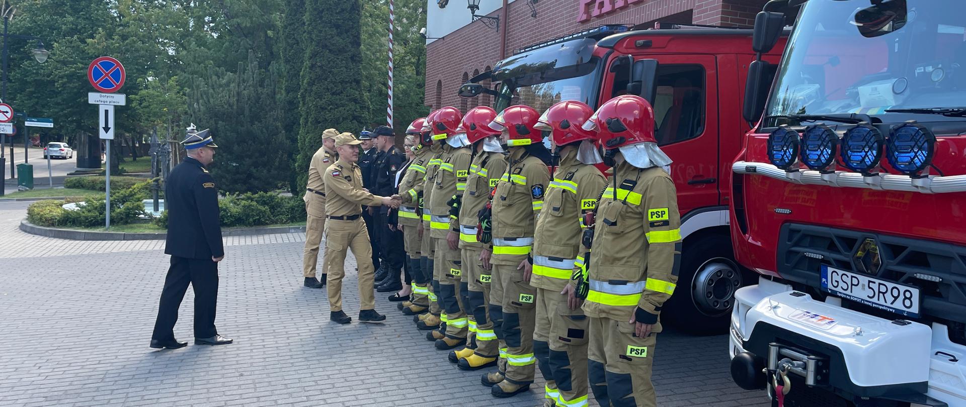Komendant Główny oraz Pomorski Komendant Wojewódzki Państwowej Straży Pożarnej wita się ze strażakami stojącymi w szeregu przed samochodami gaśniczymi