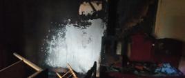Zdjęcie przedstawia pomieszczenie po pożarze. Na zdjęciu widnieją zniszczone meble oraz okopcone ściany.
