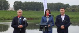 3 osoby stojące przed mikrofonami, za nimi znajduje się rzeka Odra