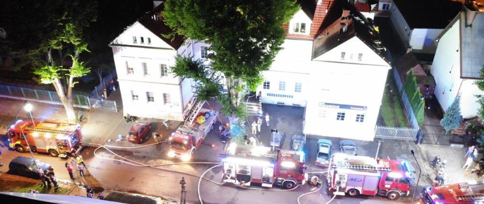 Zdjęcie z drona na którym widać pięć samochodów strażackich przed budynkiem, w którym zaistniał pożar.