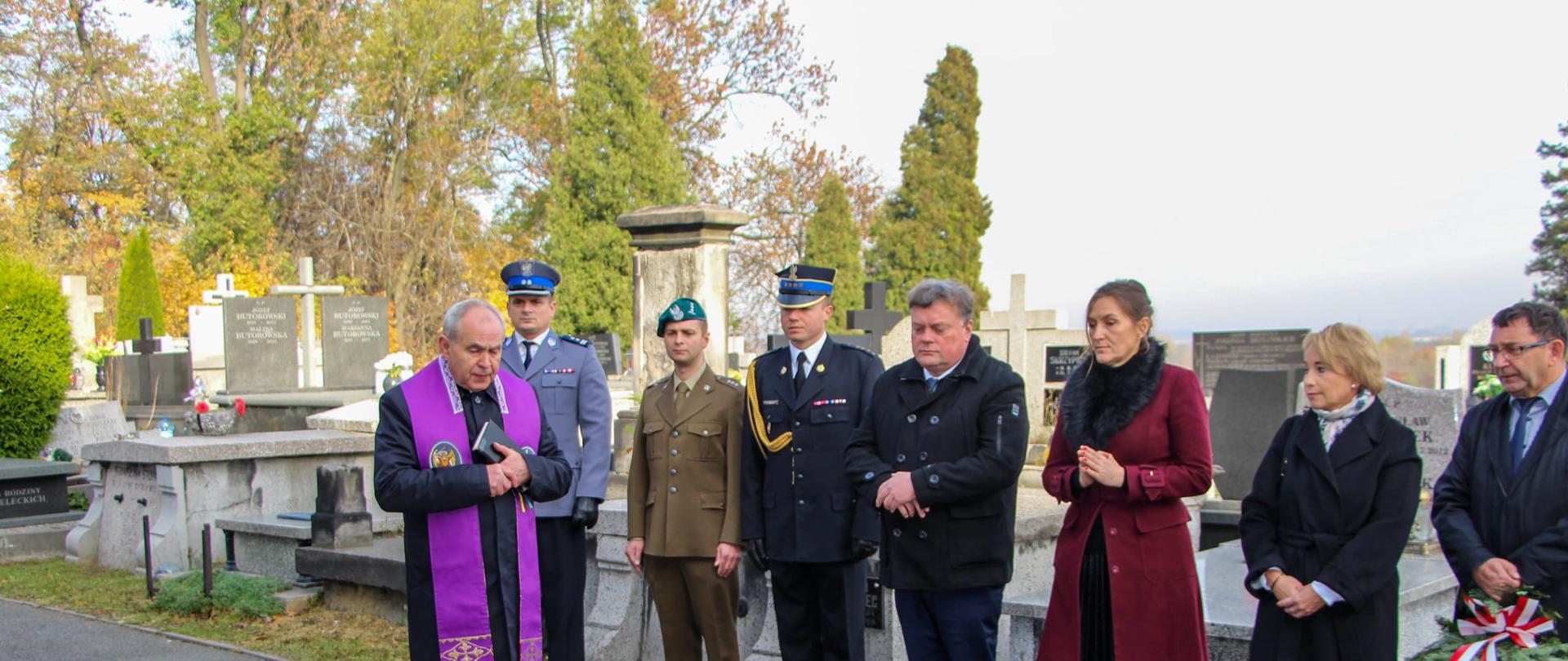 Zdjęcie ukazuje przedstawicieli samorządu oraz służb mundurowych przy grobach na terenie cmentarza parafii pw. Świętej Trójcy w Będzinie 