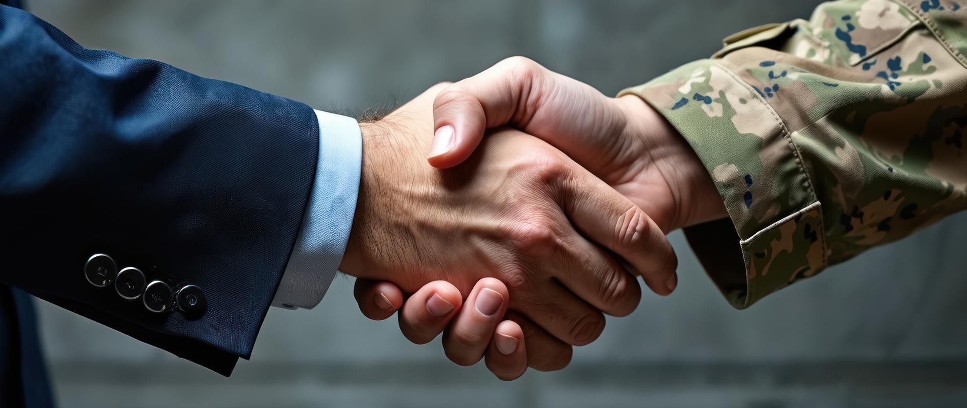 Biznesmen w garniturze ściska dłoń żołnierzowi w mundurze maskującym. Symbol współpracy między sektorem cywilnym i wojskowym.