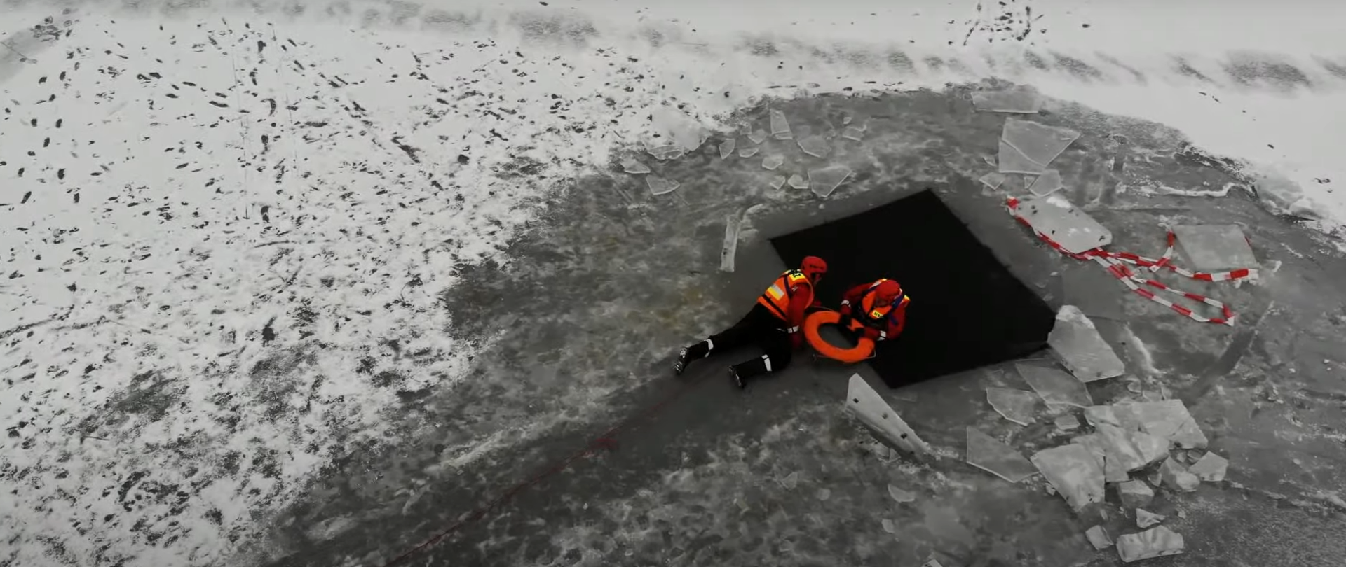 Na zdjęciu dwóch funkcjonariuszy Państwowej Straży Pożarnej na zamarzniętym akwenie wodnym podczas ćwiczeń związanych z ratownictwem lodowym.