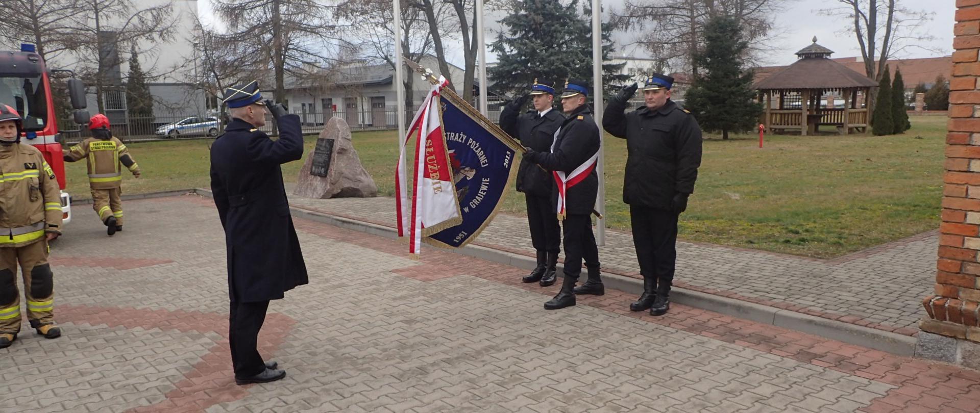 mł. bryg. Arkadiusz Lichota salutuje żegnając się z pochylonym przez poczet sztandarowy sztandarem komendy.