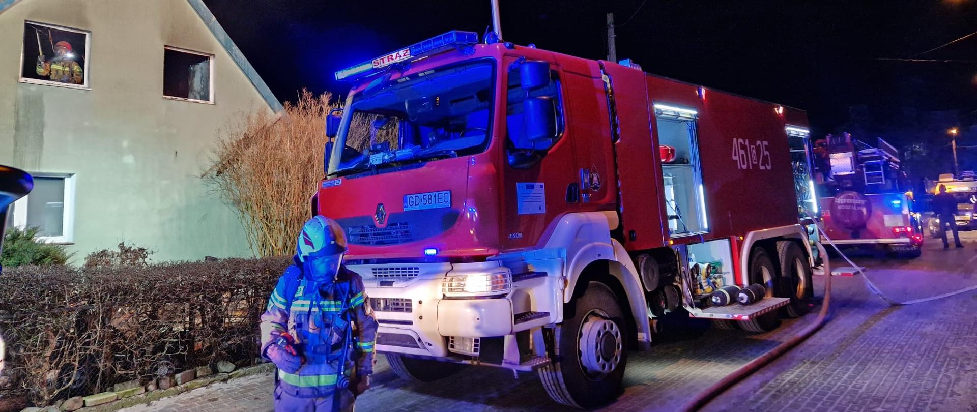 Samochód ratowniczo-gaśniczy stoi na ulicy, na pierwszy planie strażak
